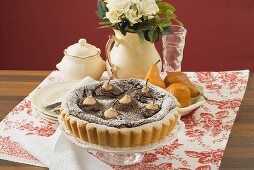 Pear and chocolate tart on cake stand, jug of roses
