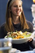 A smilling young woman holding a plate of bread salad with fennel and mandarins