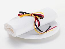 White fabric napkin tied with ribbon in colours of German flag