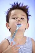 Kleiner Junge hält Joghurtlöffel im Mund