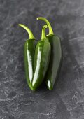 Three green jalapeño chillies on slate background