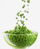 Peas falling into water in glass bowl