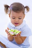 Little girl holding slice of bread with quark, cucumber and radishes