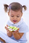 Kleines Mädchen hält Quarkbrot mit Gurken und Radieschen