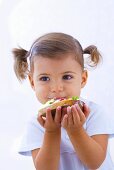 Little girl eating slice of bread with quark, cucumber and radishes