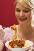 Blond woman eating spaghetti with tomato sauce