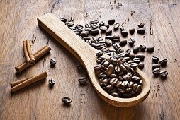 Coffee beans, wooden spoon and cinnamon sticks on wooden background