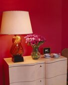Tischlampe mit Glasfuss und pinkfarbene Anemonen vor magentafarbener Wand