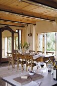 Long dining table and chairs in front of cupboard with mirrored doors and open French windows leading to terrace and garden