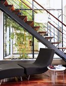 Couch and metal staircase with wooden treads in front of tall glass wall with metal frame
