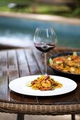 Paella and a glass of red wine by a swimming pool