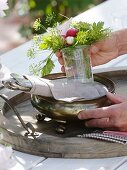 A bunch of fennel, radishes, mallow and parsley being placed on a silver dish