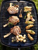 Barbecued veal chops, potatoes and pearl onions on barbecue