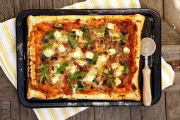 Pizza topped with feta and rocket on baking tray