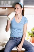 Junge Frau trinkt aus Milchflasche in der Küche