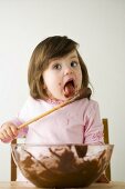Small girl licking wooden spoon