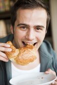 Young man biting into a croissant