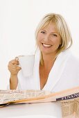 Blond woman with a cup of cappuccino reading newspaper