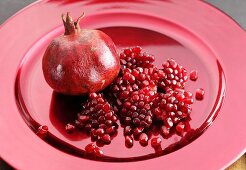 A pomegranate and pomegranate seeds on a red plate