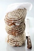 A stack of three loaves of bread with a cloth and a knife