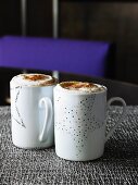 Two mugs of espresso with whisky, whipped cream & cinnamon