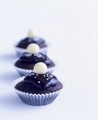 Three iced chocolate cupcakes with silver dragées