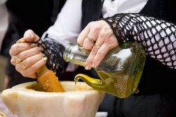 Frau in Tracht giesst Olivenöl in Mörser