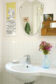A vase of flowers on a wash basin and a mirror on a white-tiled wall