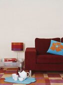 Eine rote Couch und blaues Tablett mit Teekanne und Tassen auf bunt kariertem Teppich