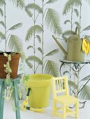 Chair, watering can and gardening tools in front of patterned wallpaper
