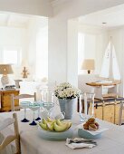 Stacked plates, flowers in zinc pot, fruit, pastries and cocktails on dining table in room with maritime decor