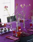 Gedeckter Tisch mit lila Tischdecke und Sommerblumendeko