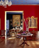 Room with gilt ornamentation, round table with marble top, bouquet of bird of paradise flowers and view into opulent dining room with large wall hanging