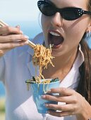 A young woman eating fried, oriental noodles with chopsticks