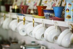 Porcelain cups hanging on a wall shelf in a kitchen