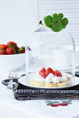 A waffle with cream and strawberries under a cloche