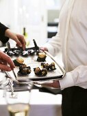 Waiter serving tray of bacon-wrapped prunes at champagne reception