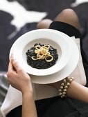 Woman holding plate of squid ink risotto