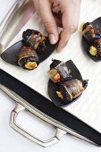 Hand reaching for bacon-wrapped prunes stuffed with goat's cheese