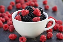 Blackberries and raspberries in and around a cup