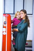 Mutter mit kleiner Tochter auf dem Arm neben Kühlschrank