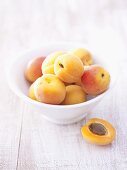 Several apricots in bowl, half an apricot beside it
