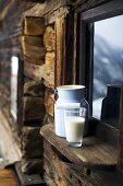 Milchkanne und Milchglas auf Fensterbrett einer Almhütte