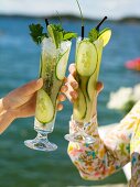 Two women raising glasses of cucumber drink (out of doors)