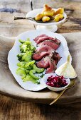 Slices of roast beef with cucumber salad, salsa and potatoes