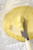 Farmhouse butter on paper with butter knife (close-up)