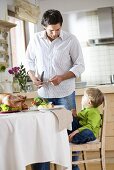 Father standing, son sitting at laid table