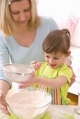 Mother and daughter sieving flour into a bowl