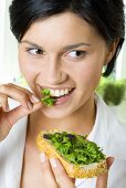 Young woman eating a slice of bread topped with herbs