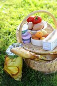 Picnic basket filled with fruit, eggs, cream cheese, baguette, etc